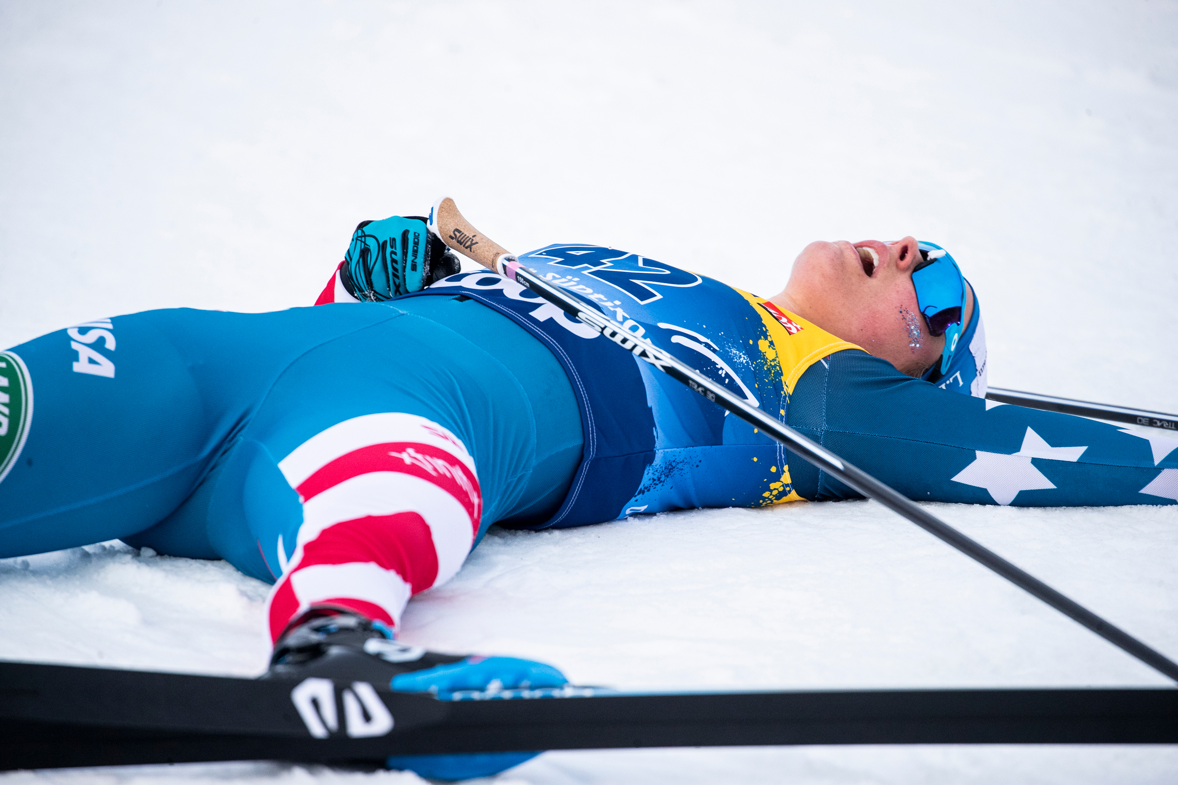 An exhausted Jessie Diggins lies on the snow after crossing the finish line in Tuesday's third stage of the Tour de Ski.  (www.nordicfocus.com. © Modica/NordicFocus)