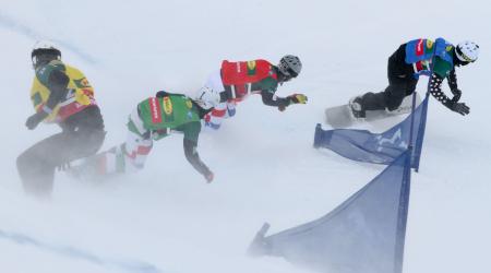 Four snowboard cross racers round a gate. 